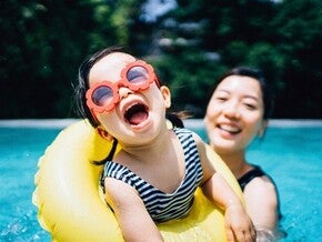 Photo of a child and mother in a pool; one in a yellow tube wearing a striped swimsuit