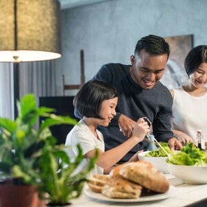 Photograph: Smiling family making salad together in bright kitchen