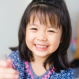 Smiling young girl in blue patterned shirt reaching toward camera