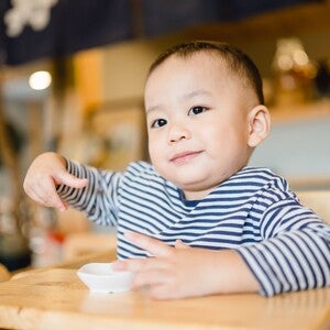 Photo of a toddler in blue-striped shirt at café table holding a spoon