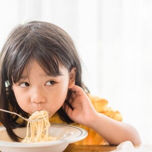 Photograph: girl in yellow shirt eating noodles with chopsticks, glancing sideways