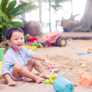 Photo of a toddler in a sandbox playing with colorful plastic buckets and toys