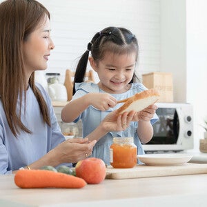 Photo of smiling mother and daughter preparing bread together in a bright kitchen