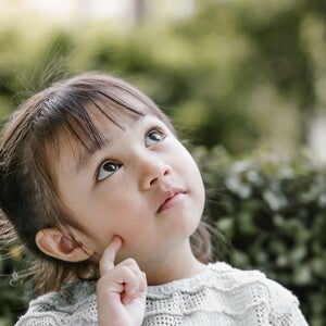 Thoughtful young girl with braided pigtails looking up against leafy background