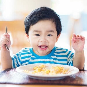 Photo: young child in blue-striped shirt raising a fork over a plate of pasta