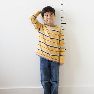 Photograph — smiling boy in yellow striped shirt by height chart, hand on head