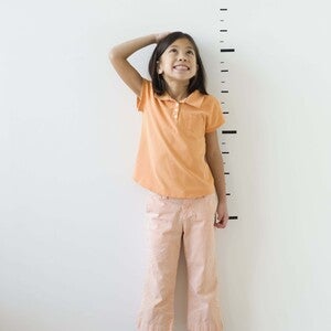 Photo: smiling girl in orange shirt and pink pants in adult heels beside height marks