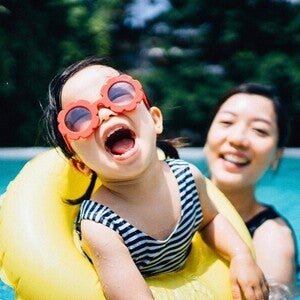 Photo of a child and mother in a pool; one in a yellow tube wearing a striped swimsuit
