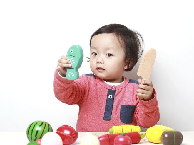 Photograph of a toddler, holding a toy dinosaur and wooden spatula