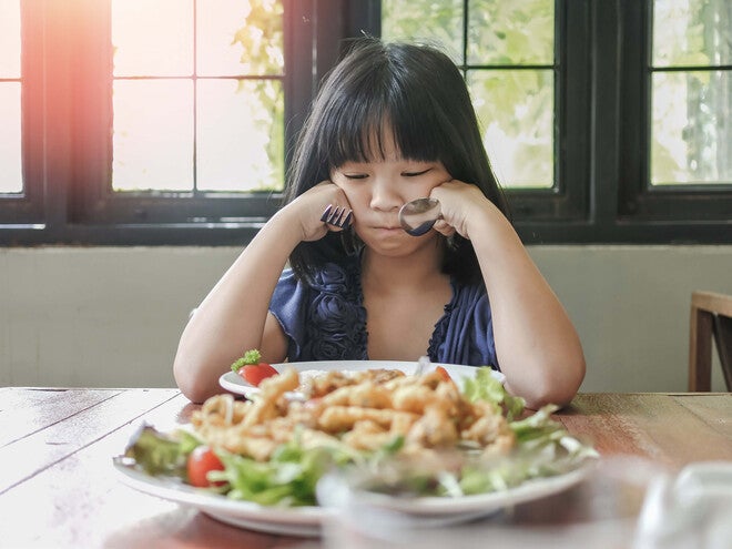 Photograph of a young girl rubbing her eyes at a table with a plate of shrimp salad