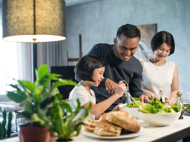 Photograph: Smiling family making salad together in bright kitchen