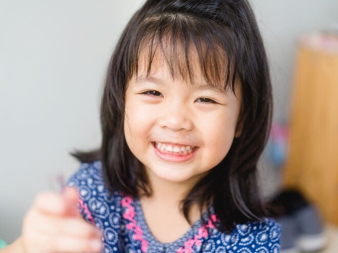 Smiling young girl in blue patterned shirt reaching toward camera