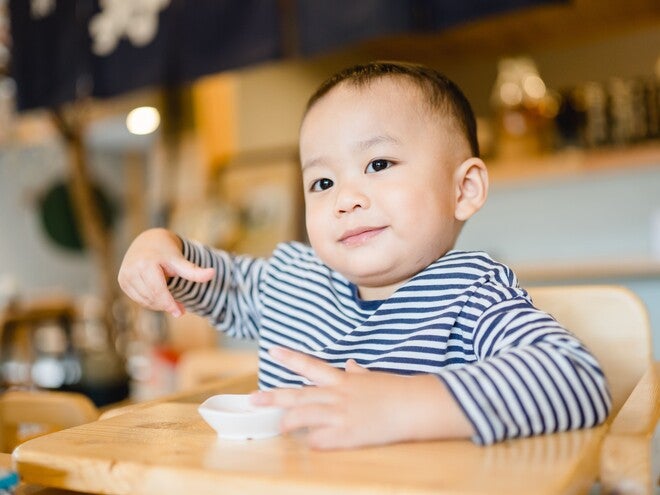 Photo of a toddler in blue-striped shirt at café table holding a spoon