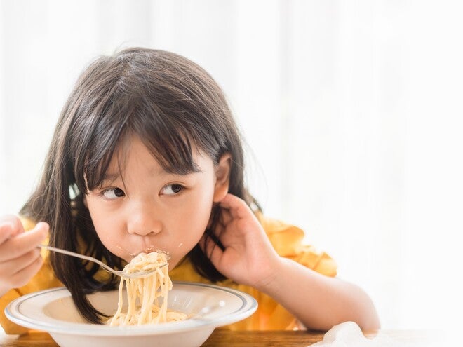 Photograph: girl in yellow shirt eating noodles with chopsticks, glancing sideways