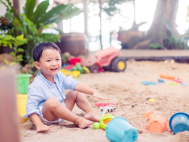 Photo of a toddler in a sandbox playing with colorful plastic buckets and toys