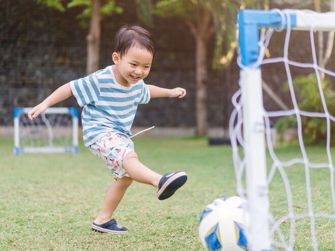 Smiling boy kicking soccer ball toward small backyard goal