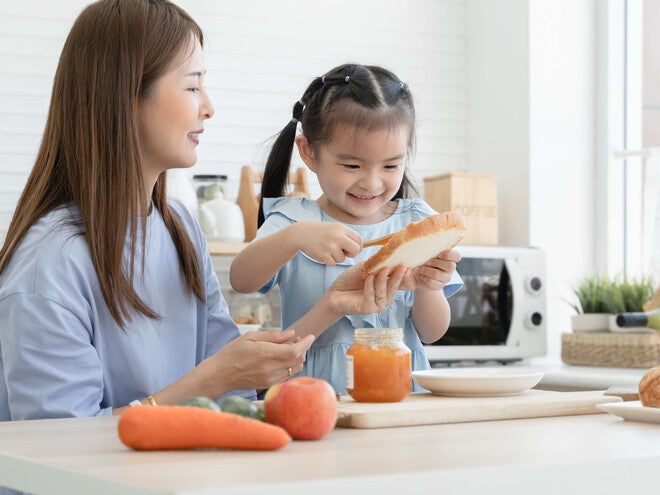 Photo of smiling mother and daughter preparing bread together in a bright kitchen