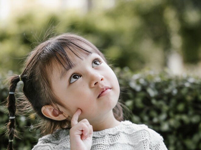 Thoughtful young girl with braided pigtails looking up against leafy background