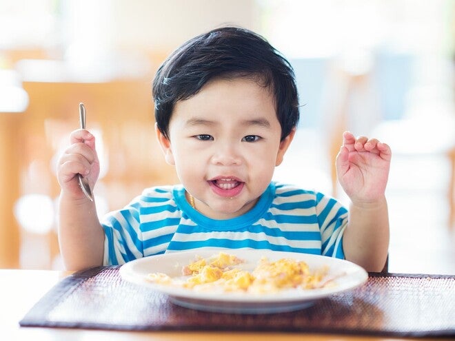 Photo: young child in blue-striped shirt raising a fork over a plate of pasta
