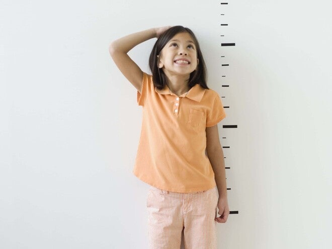 Photo: smiling girl in orange shirt and pink pants in adult heels beside height marks